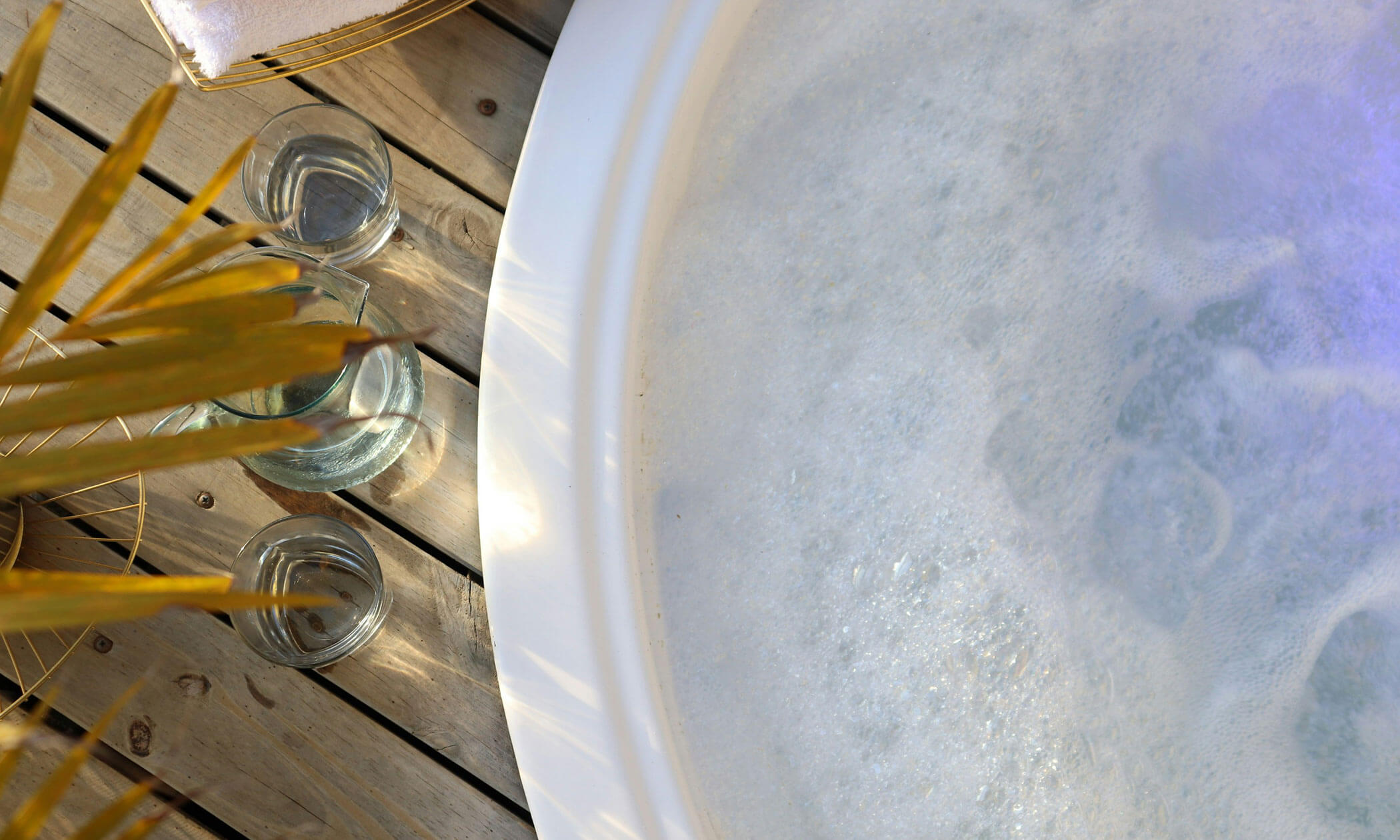 Ein sprudelnder Whirlpool auf einer Holzterrasse, daneben zwei Gläser Wasser und eine Pflanze. - Lüch de Poldele