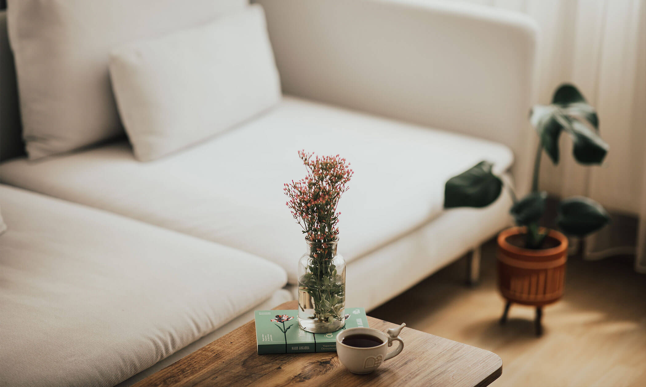 Ein gemütliches Wohnzimmer mit einem weißen Sofa, einem Holztisch, Blumen in einer Vase und einer Tasse Kaffee. - Lüch de Poldele