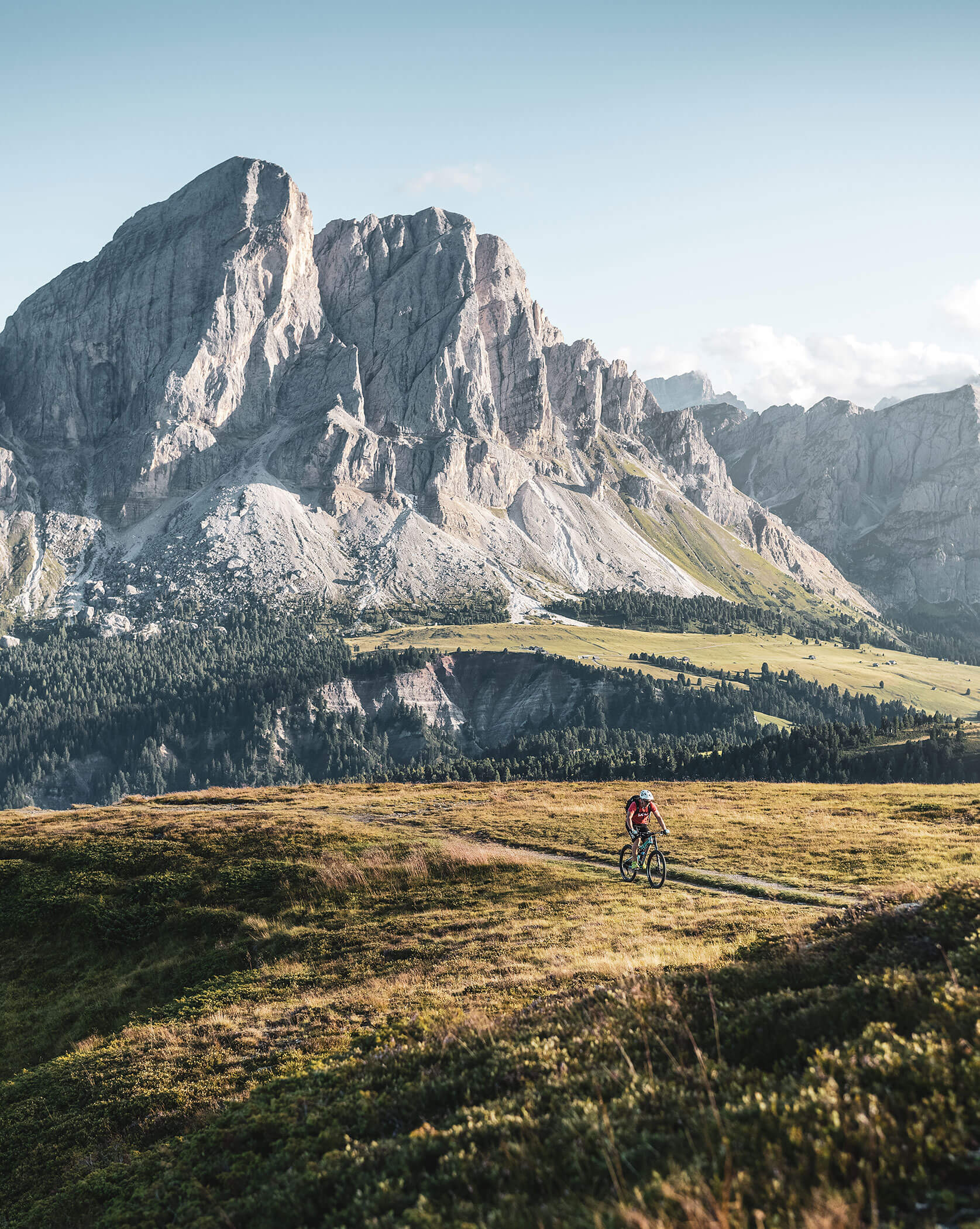 Eine Person fährt mit dem Fahrrad auf einem grasbewachsenen Weg, im Hintergrund ist ein hoher Berg zu sehen, und der Himmel ist klar. - Lüch de Poldele