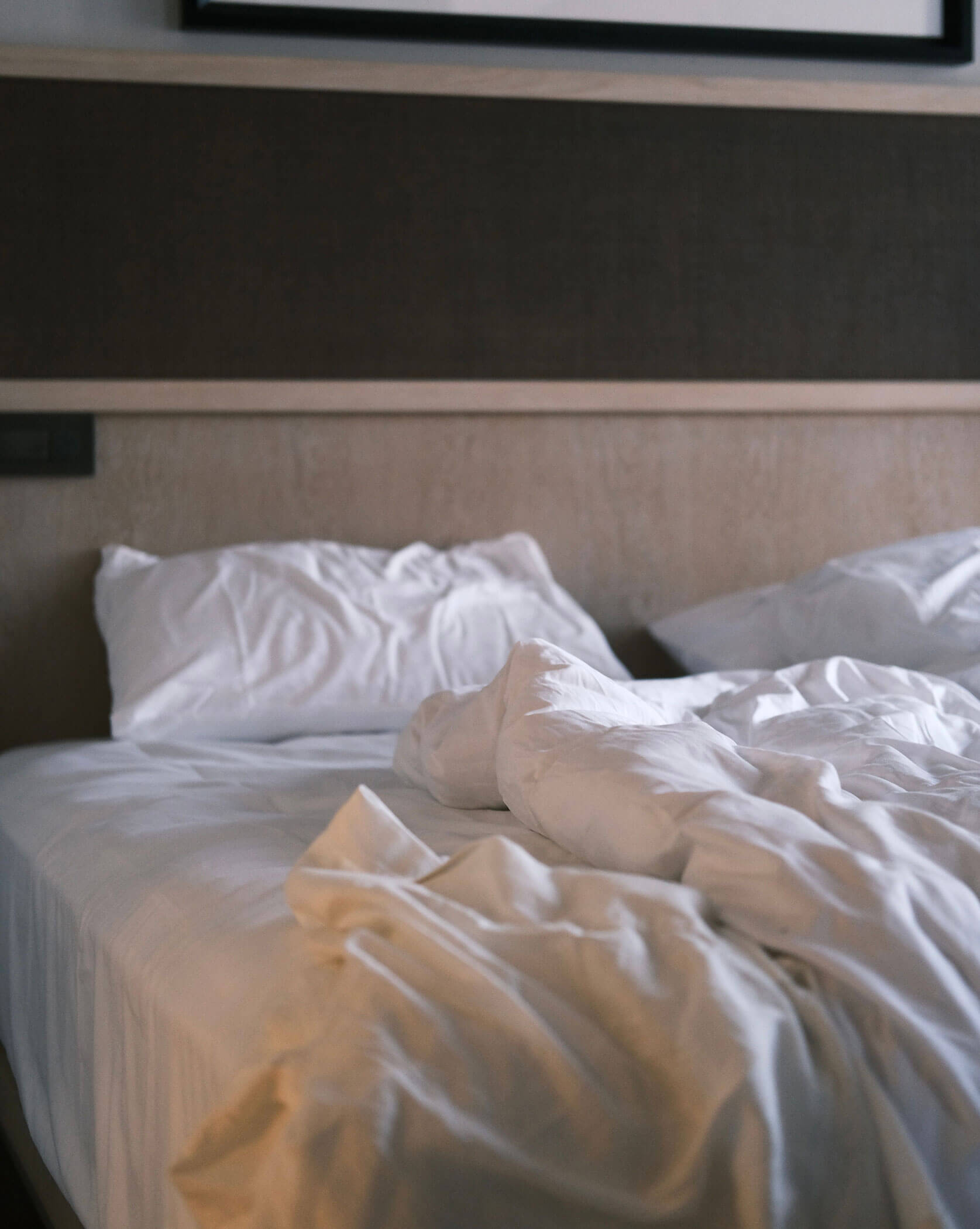 Ein ungemachtes Bett mit weißer Bettwäsche und Kissen in einem sanft beleuchteten Raum. - Lüch de Poldele