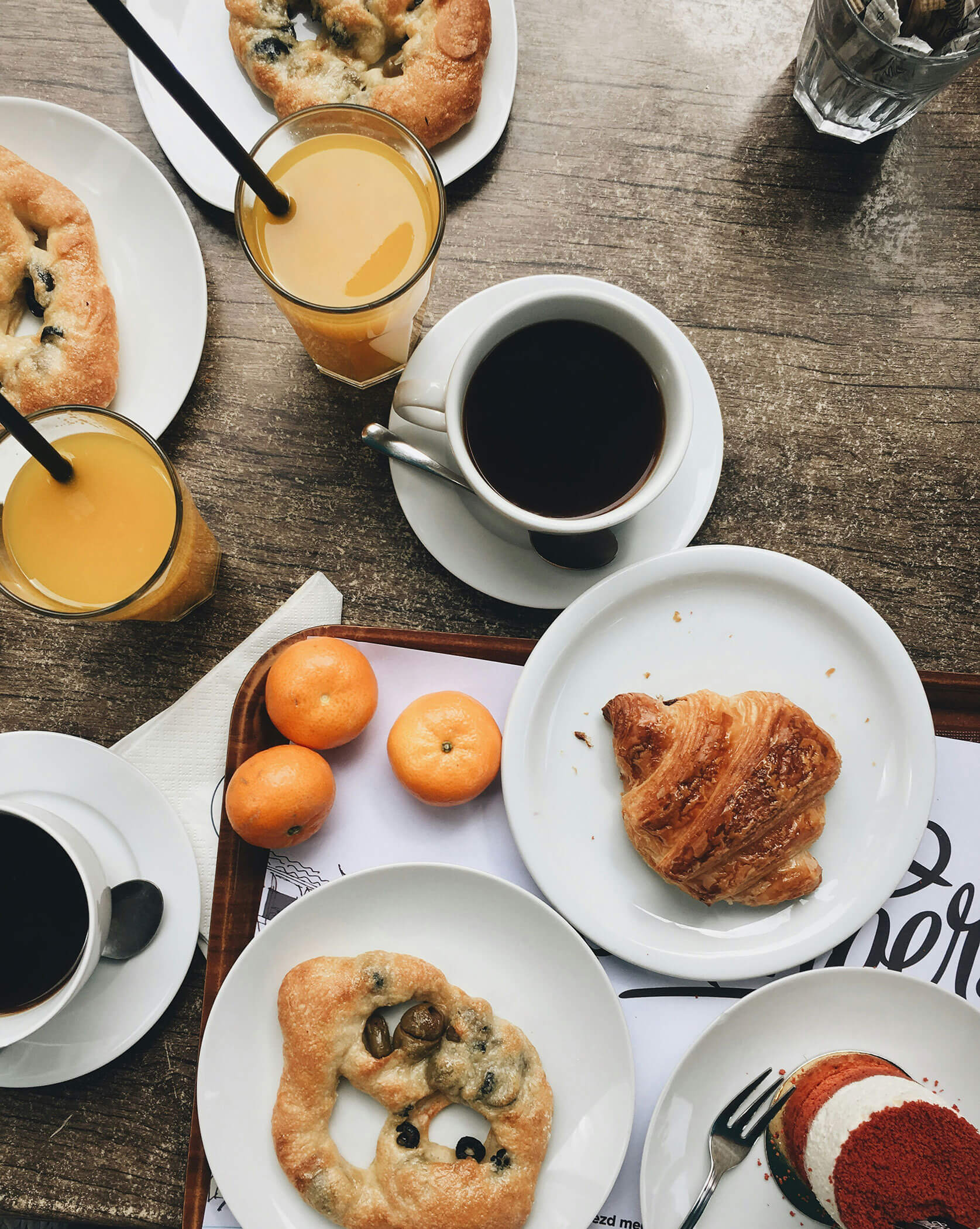 Frühstückstisch mit Kaffee, Orangensaft, Gebäck, Mandarinen und Kuchen auf weißen Tellern. - Lüch de Poldele