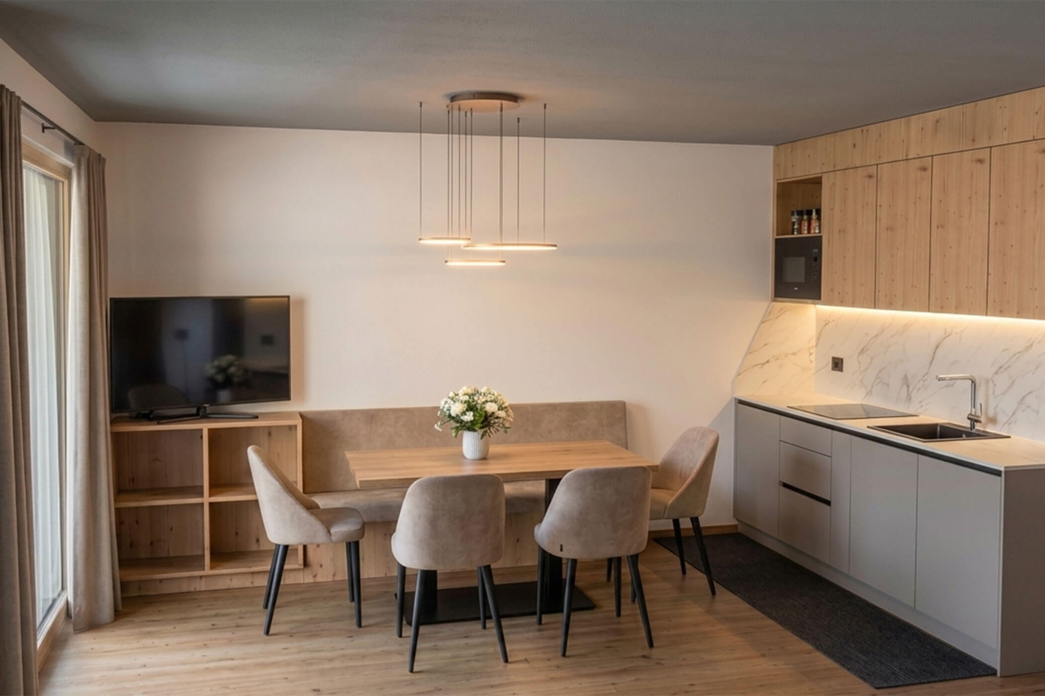 Moderne Küche und Essbereich mit einem Holztisch, vier Stühlen, einem Fernseher und minimalistischer Einrichtung. - Lüch de Poldele